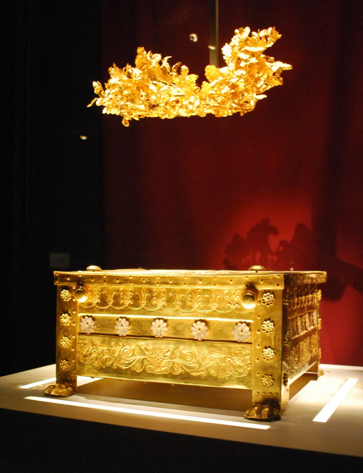 The gold larnax of Tomb II, its lid embossed with the 16-ray Vergina Sun, with a gold wreath displayed above it.